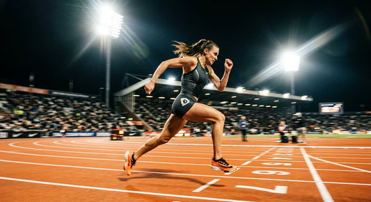 Professional high-speed action shot of a runner sprinting on a track under dramatic stadium floodlights with motion blur.