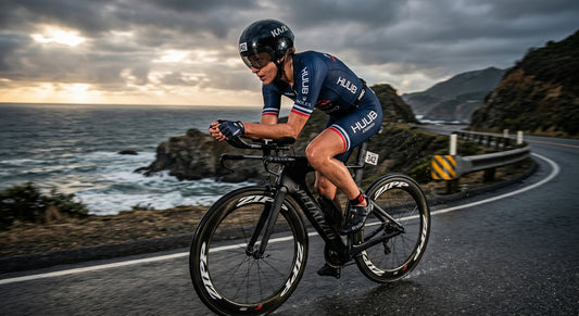 A professional triathlete in a sleek aero trisuit cycling at high speed on a coastal road with dramatic stadium-like cinematic lighting.