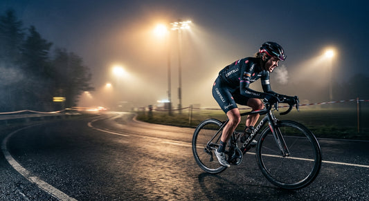 A professional cyclist sprinting through a misty, cold morning road with dramatic stadium lighting and high-speed motion blur.