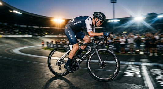 Professional cyclist in a high-speed aerodynamic tuck, illuminated by dramatic stadium lighting with motion blur on the wheels.