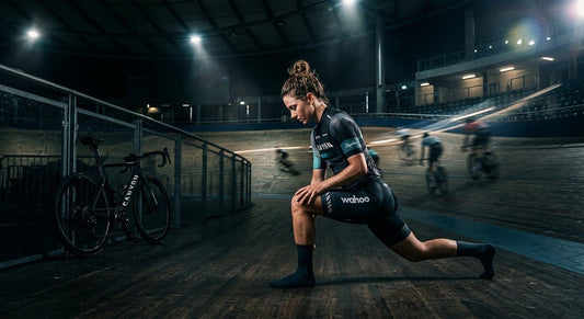 A professional cyclist performing a deep lunge stretch in a moody, cinematic stadium environment with dramatic lighting and motion blur