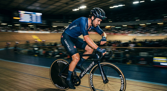 A professional cyclist in a dark, moody stadium setting checking a heart rate monitor with high-speed motion blur.