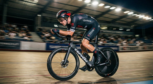 A professional cyclist in an aerodynamic tuck position on a carbon fibre frame, captured with high-speed motion blur and dramatic stadium lighting.