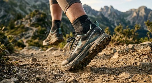 A close-up action shot of an athlete's feet wearing Altra Lone Peak 10s, showing the wide toe box and rugged outsole on a dusty mountain trail.