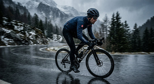 A professional cyclist wearing a Castelli Perfetto RoS 2 jacket, captured in a high-speed motion blur during a rainy winter training session on a desolate mountain road.