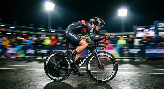 A professional cyclist in a time-trial position, captured with high-speed motion blur, illuminated by dramatic stadium lighting during a night race.