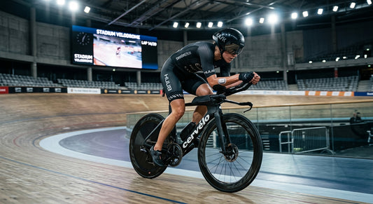 Professional triathlete cycling in a high-speed aero position with a CGM sensor visible on the arm, captured in dramatic stadium lighting.