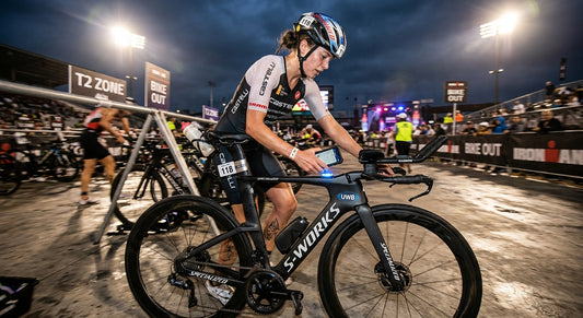 A professional triathlete in a high-speed transition zone, using a smartphone to scan a UWB-enabled tracking tag on a carbon fibre bike frame under dramatic cinematic stadium lighting.