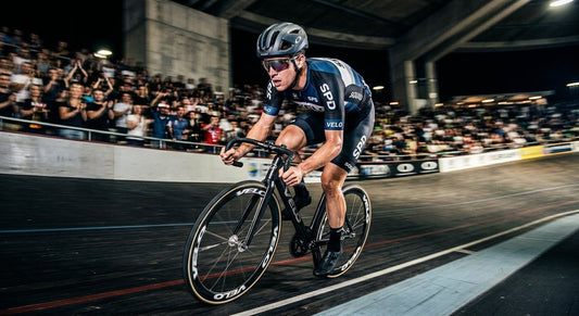 Professional cyclist wearing Oakley Sphaera Strike sunglasses during a high-speed sprint in a stadium, featuring motion blur and sharp contrast.