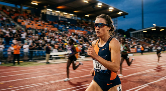 A close-up, high-speed action shot of a professional runner wearing sleek, aerodynamic sports sunglasses during a twilight stadium race with motion blur.