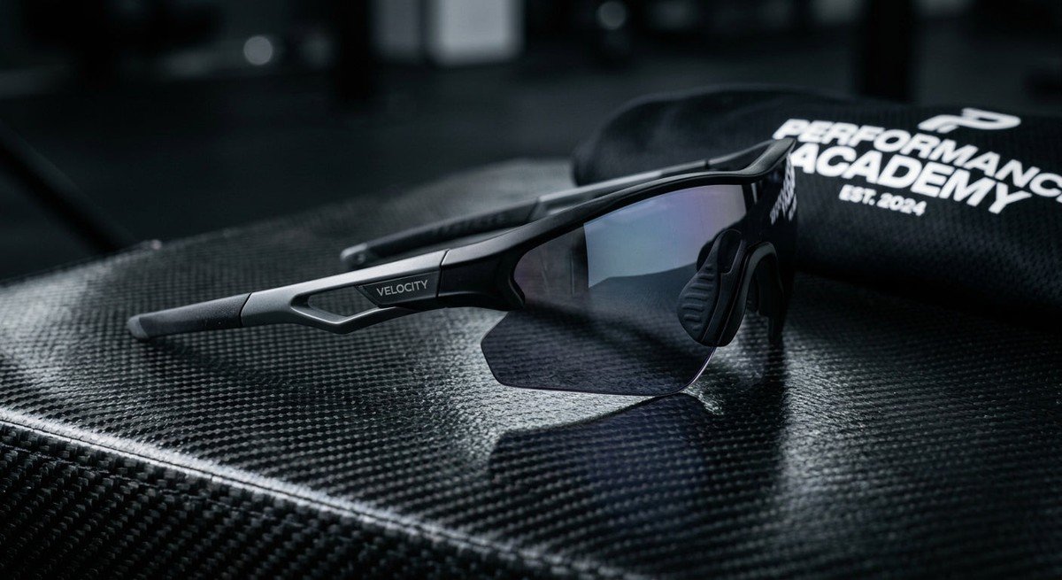 A close-up of high-performance aerodynamic sunglasses resting on a carbon fibre surface with dramatic studio lighting.
