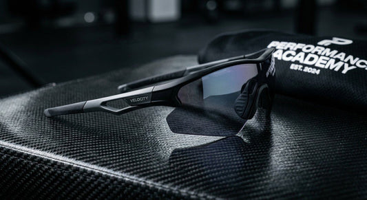 A close-up of high-performance aerodynamic sunglasses resting on a carbon fibre surface with dramatic studio lighting.