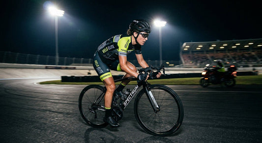 Professional cyclist wearing Tifosi Moab photochromic shield glasses during a high-speed road training session under dramatic stadium lighting.