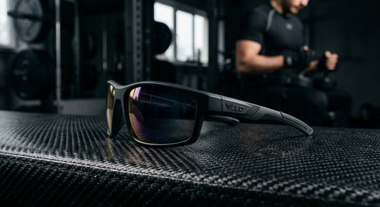 A close-up of high-performance sports sunglasses resting on a carbon fibre surface with dramatic studio lighting.