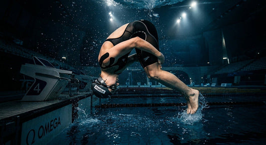 A professional swimmer wearing Form Smart Swim Goggles 2 performing a flip turn in a moody, high-contrast aquatic centre with cinematic lighting.