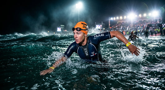 A professional triathlete performing a sighting stroke in choppy ocean water with dramatic stadium-style lighting.