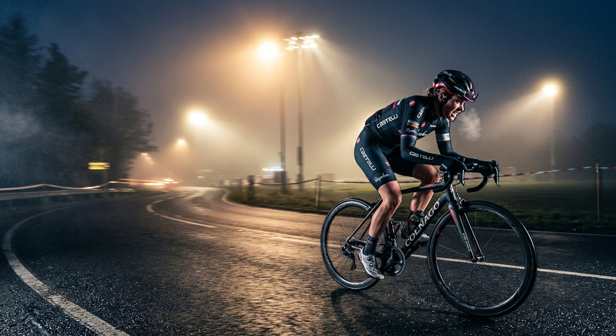 A professional cyclist sprinting through a misty, cold morning road with dramatic stadium lighting and high-speed motion blur.