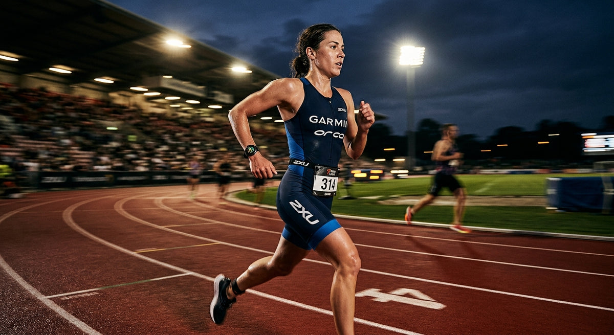 A professional triathlete wearing a high-end multisport GPS watch during a high-intensity track session, captured with motion blur and dramatic stadium floodlighting.