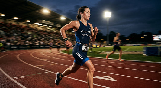 A professional triathlete wearing a high-end multisport GPS watch during a high-intensity track session, captured with motion blur and dramatic stadium floodlighting.
