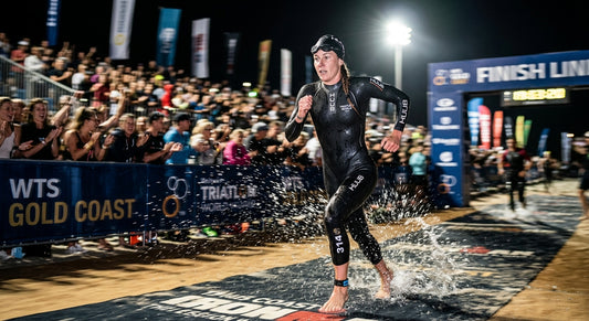 A professional triathlete in a sleek black wetsuit sprinting out of the water with dramatic stadium lighting and high-speed motion blur.