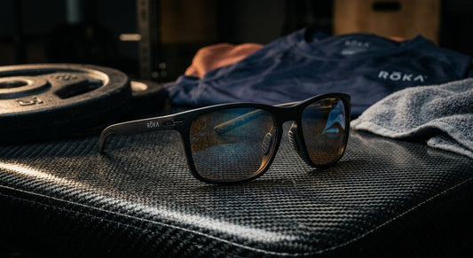 A close-up shot of the ROKA Rory 2.0 sunglasses resting on a carbon fibre surface with dramatic lighting highlighting the lens texture.