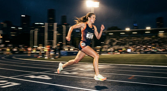 A professional runner captured in a high-speed motion blur, demonstrating a high-cadence stride on an urban track under dramatic stadium lighting.