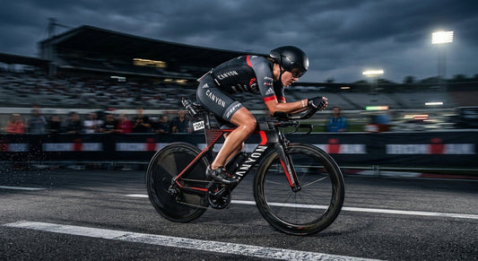 A professional triathlete in a low-crouch aerodynamic position on a carbon-fibre time trial bike, captured with high-speed motion blur against a moody stadium backdrop.