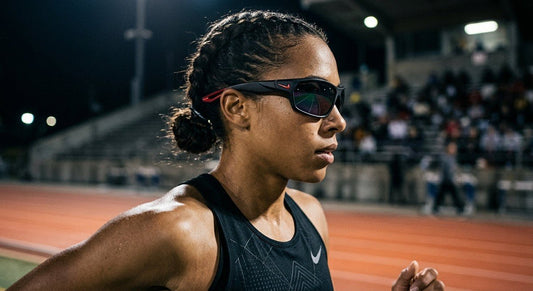 A professional close-up of the Nike Vision Windtrack Heat sunglasses showing the sleek, aerodynamic frame design under moody stadium lighting.