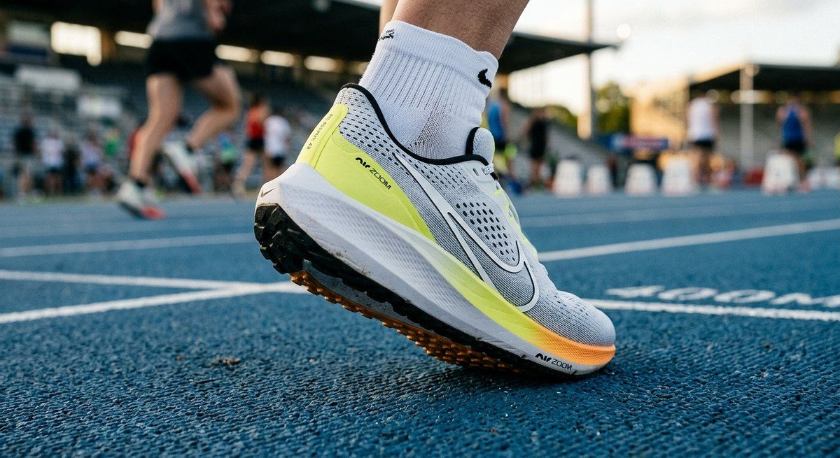 A close-up of the Nike Pegasus 42 silhouette in motion, capturing the textured mesh upper and the sleek, aerodynamic heel counter against a blurred stadium track background.