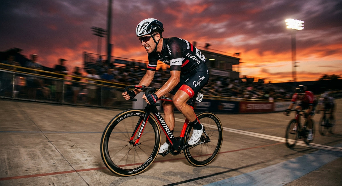 A professional road cyclist sprinting with intense focus, captured in high-speed motion blur against a dramatic, moody sunset background at a velodrome.