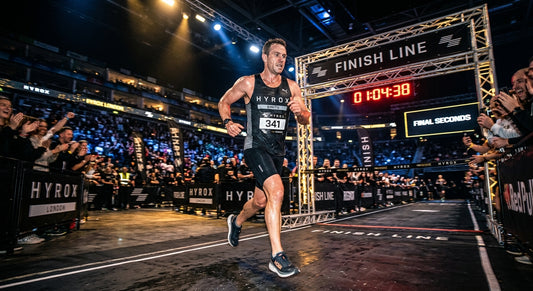 A professional athlete in the final seconds of a Hyrox race, captured with cinematic stadium lighting and high-speed motion blur.