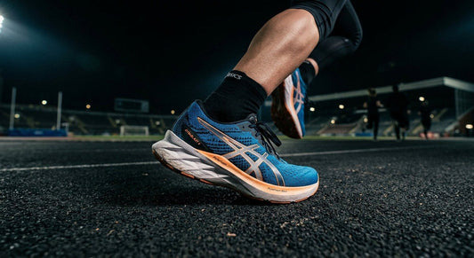 A close-up shot of the Asics Dynablast 6 featuring a sharp focus on the textured knit upper and the high-rebound midsole foam in a dramatic, dark stadium setting.