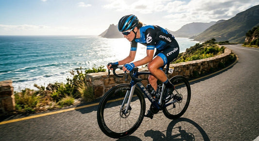 Professional cyclist in an aerodynamic tuck position on a road bike during a high-speed training session on a sun-drenched coastal road.