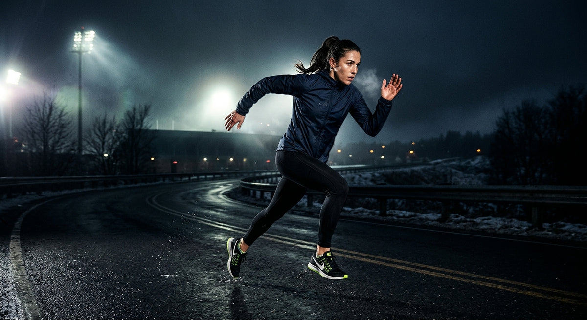 Professional high-speed athletic action photography of a runner on a dark winter road with moody dramatic contrast and cinematic stadium lighting.