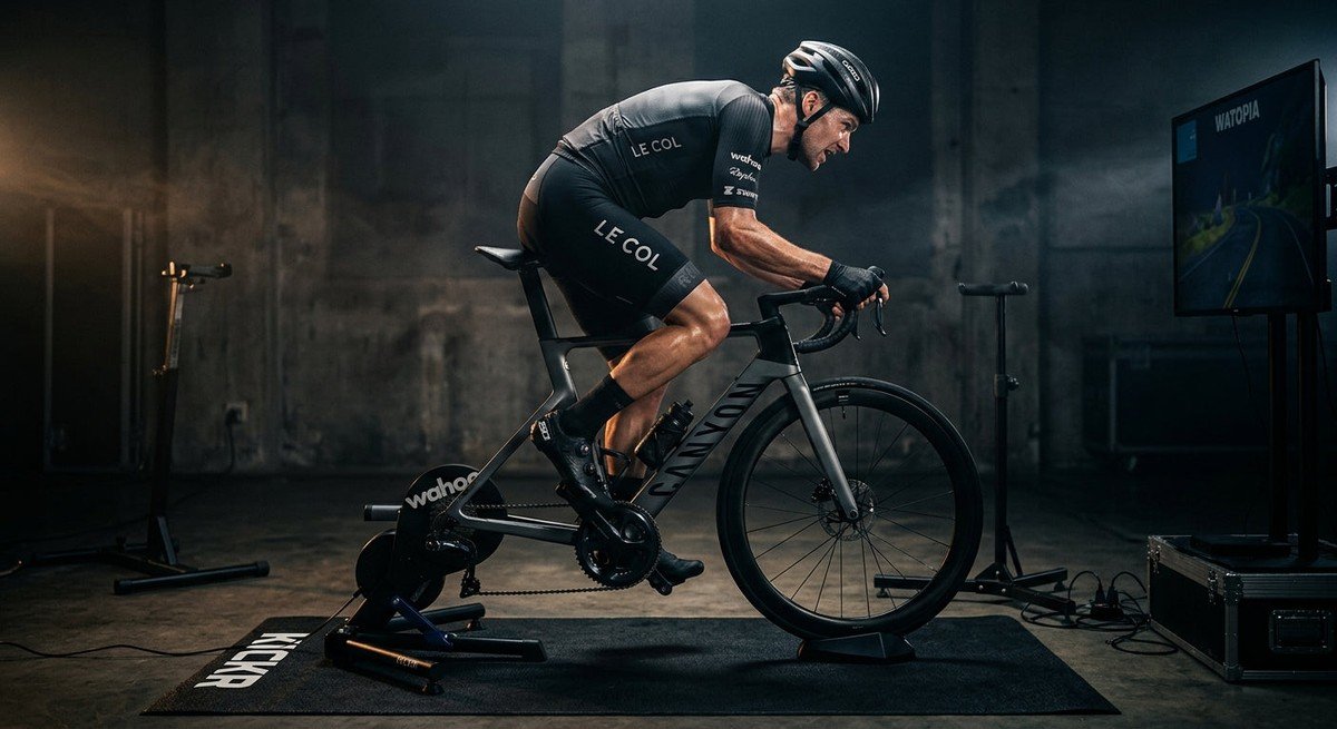 A professional cyclist sprinting on a Wahoo Kickr in a darkened studio with dramatic cinematic lighting.