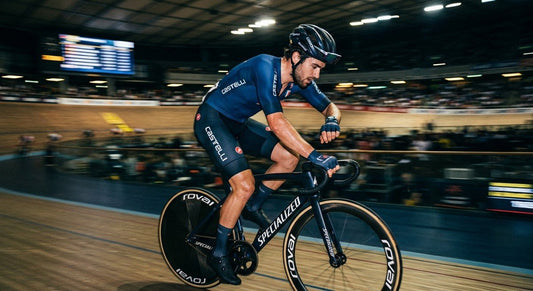 A professional cyclist in a dark, moody stadium setting checking a heart rate monitor with high-speed motion blur.