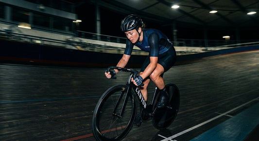 A professional cyclist in a darkened velodrome, focused on a head unit displaying real-time power and heart rate data, cinematic lighting.