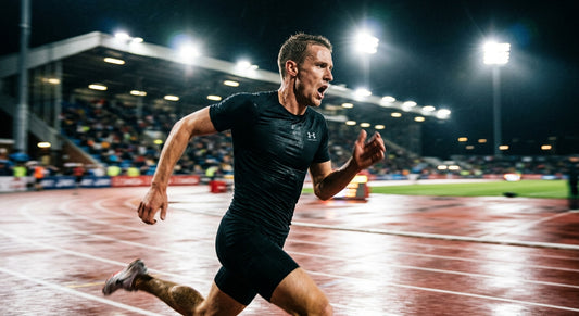 A professional endurance athlete in a high-speed motion blur, gasping for air while wearing a sleek, dark performance base layer under dramatic stadium lighting.