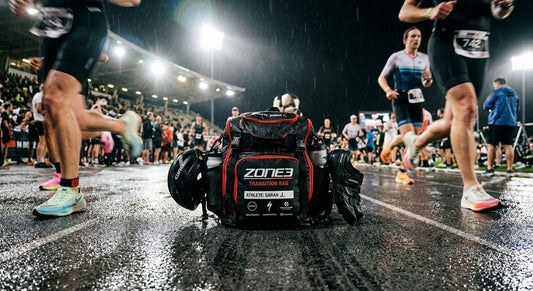 A close-up of a high-performance triathlon transition bag on a wet track with dramatic stadium lighting and high-speed motion blur.