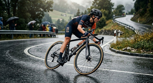 A professional cyclist performing a high-speed corner on a damp road, highlighting the contrast of modern road tyres against the tarmac.