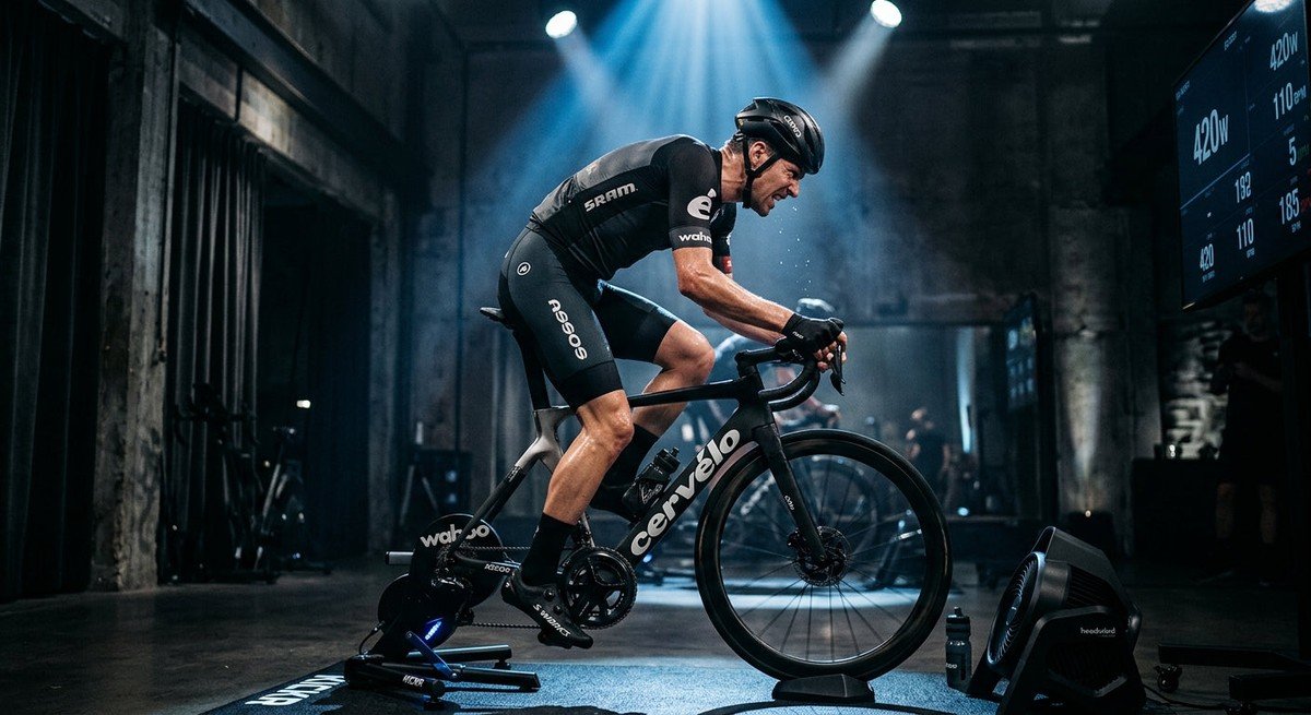 Professional cyclist performing a high-intensity interval session on a smart trainer in a dark, moody studio with cinematic stadium lighting.
