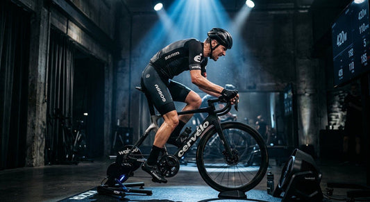 Professional cyclist performing a high-intensity interval session on a smart trainer in a dark, moody studio with cinematic stadium lighting.