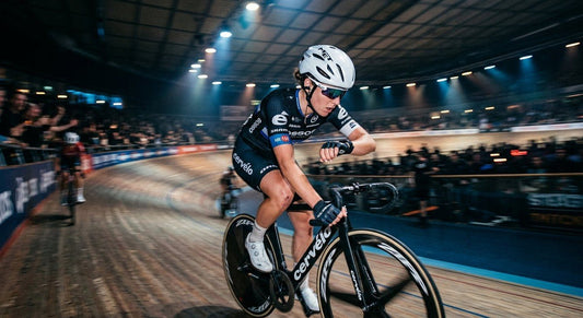 A professional cyclist in moody stadium lighting checking their heart rate monitor, showcasing high-speed action blur.