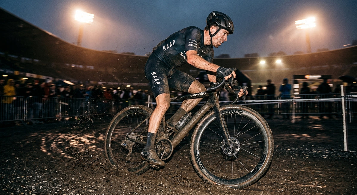 Professional high-speed athletic action photography of a gravel cyclist riding ENVE G SES wheels through mud with moody cinematic stadium lighting and sharp fine details