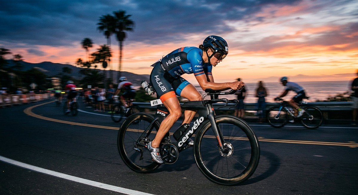 Professional triathlete in a blurred, high-speed cycling motion during a dramatic sunset race event.