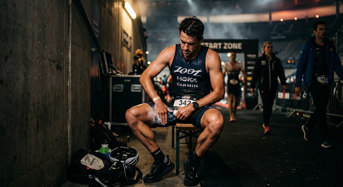 A professional triathlete applying anti-chafe balm with intense focus in a moody, cinematic stadium setting.