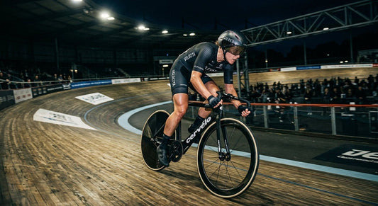 Professional cyclist in an aggressive sprint position on a velodrome track with dramatic stadium lighting.