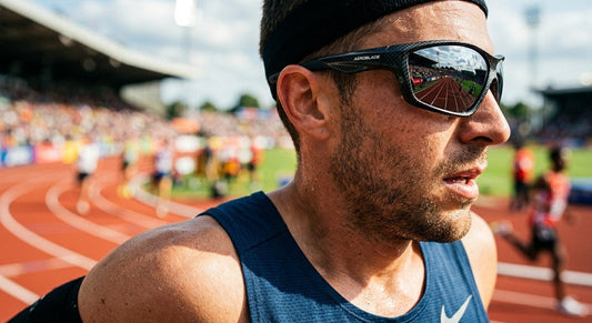 A close-up of high-performance sunglasses with a sleek, aerodynamic carbon-fibre frame reflecting a vibrant stadium track, captured in sharp focus with a shallow depth of field.