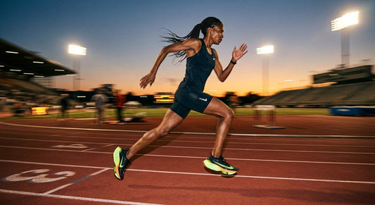 A professional long-distance runner sprinting on a track at dusk, captured with high-speed motion blur and dramatic stadium lighting illuminating the carbon-plated shoes.