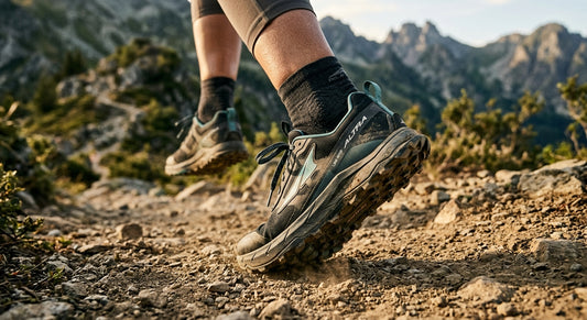 A close-up action shot of an athlete's feet wearing Altra Lone Peak 10s, showing the wide toe box and rugged outsole on a dusty mountain trail.